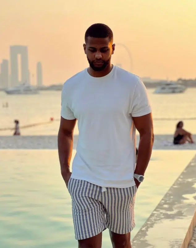 Yomi Denzel, à la Marina de Dubaï, sous un splendide coucher de soleil, portant une luxueuse montre Patek Philippe, évoquant la prospérité et l'opulence.